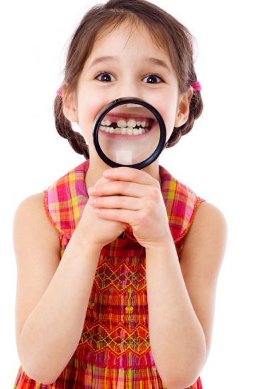 Funny girl showing teeth through a magnifying glass, isolated on white